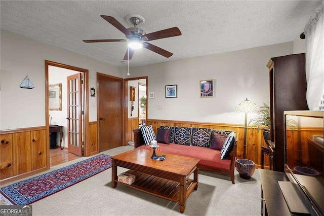 living room featuring a ceiling fan, a textured ceiling, carpet, and a wainscoted wall