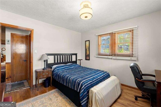 bedroom featuring baseboards, a textured ceiling, and wood finished floors