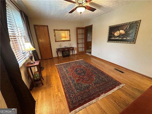 interior space featuring a ceiling fan, a textured ceiling, visible vents, and wood finished floors