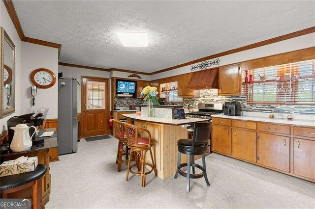 kitchen with appliances with stainless steel finishes, light floors, custom range hood, a kitchen bar, and ornamental molding