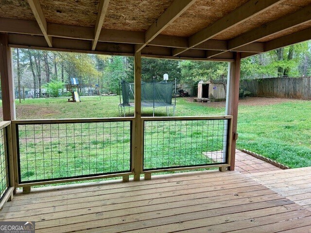 wooden deck with a trampoline, a yard, and a fenced backyard