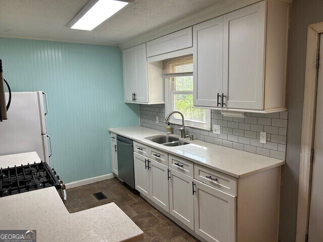 kitchen featuring freestanding refrigerator, backsplash, a sink, visible vents, and dishwasher