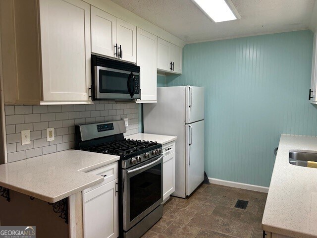 kitchen with white cabinetry, decorative backsplash, stainless steel gas range, visible vents, and freestanding refrigerator