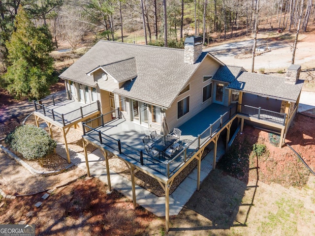 rear view of property with a shingled roof, a chimney, and a deck