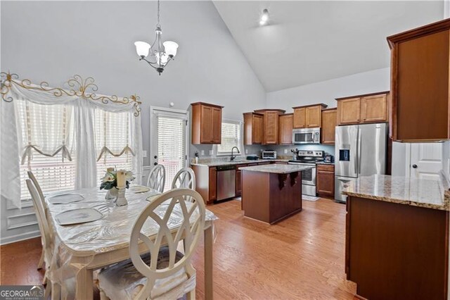 kitchen with a kitchen island, light wood finished floors, a chandelier, appliances with stainless steel finishes, and brown cabinetry