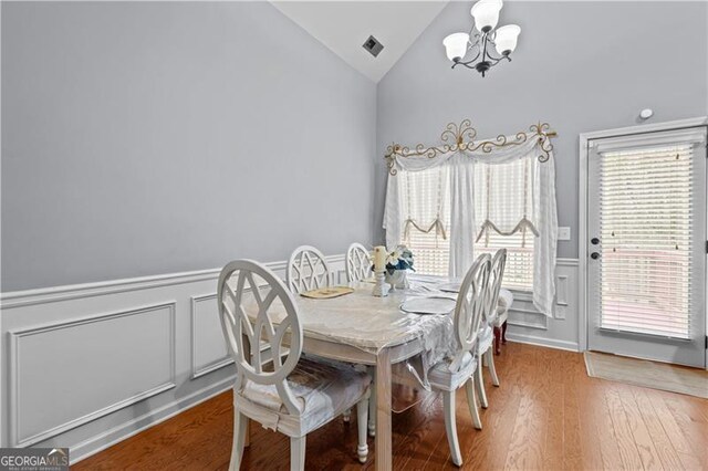 dining area featuring visible vents, wainscoting, wood finished floors, lofted ceiling, and a notable chandelier