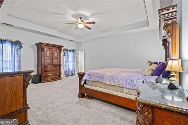carpeted bedroom featuring visible vents, a ceiling fan, and a raised ceiling