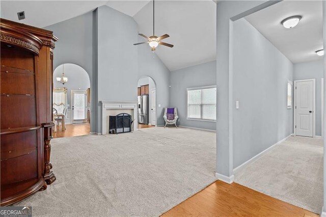 unfurnished living room featuring high vaulted ceiling, a fireplace with flush hearth, arched walkways, a ceiling fan, and light carpet