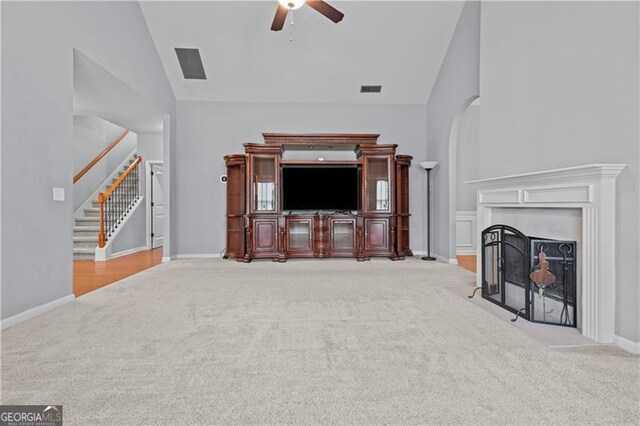 carpeted living room with a fireplace with flush hearth, baseboards, ceiling fan, and stairway