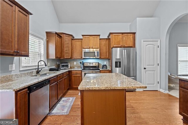 kitchen with appliances with stainless steel finishes, arched walkways, lofted ceiling, a sink, and a center island