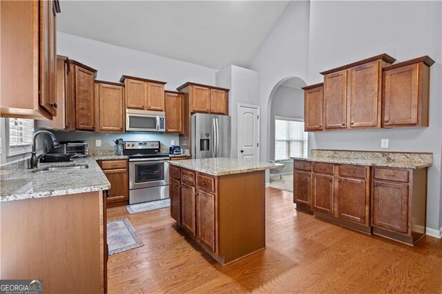 kitchen featuring a sink, arched walkways, light wood finished floors, appliances with stainless steel finishes, and brown cabinets