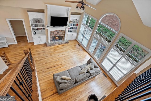 living area with ceiling fan, light wood-style flooring, visible vents, a stone fireplace, and a high ceiling