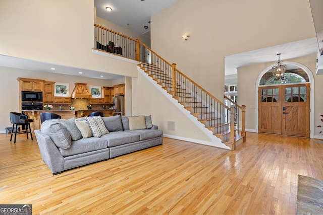 living area with an inviting chandelier, light wood-style flooring, visible vents, stairs, and baseboards