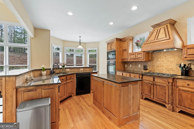 kitchen with black appliances, a sink, a center island with sink, custom range hood, and backsplash