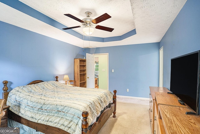 bedroom featuring a ceiling fan, a textured ceiling, light colored carpet, baseboards, and a tray ceiling