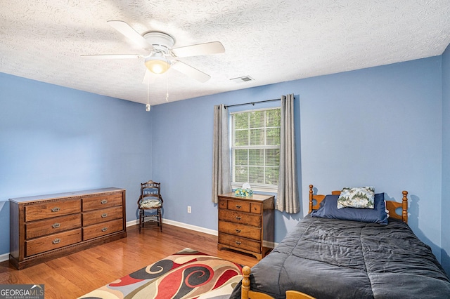 bedroom with ceiling fan, a textured ceiling, visible vents, wood finished floors, and baseboards