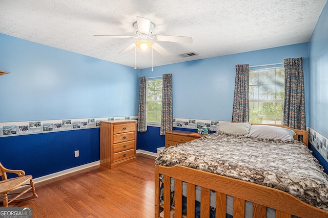 bedroom featuring baseboards, a textured ceiling, visible vents, and wood finished floors