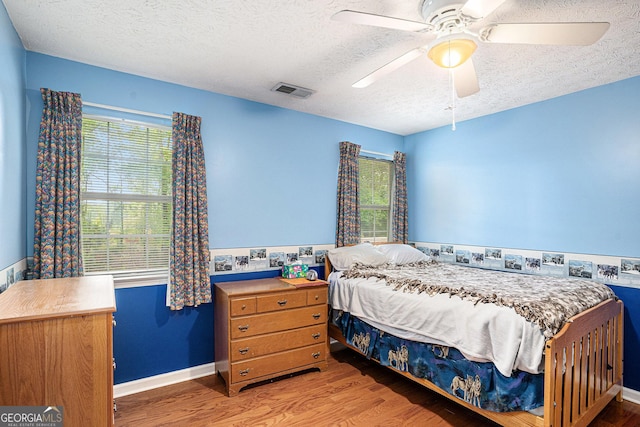 bedroom featuring visible vents, a ceiling fan, a textured ceiling, and wood finished floors