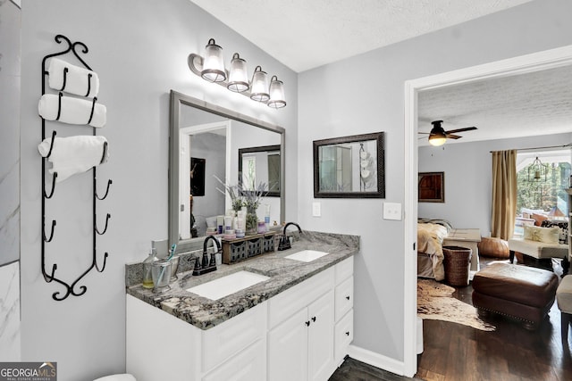 ensuite bathroom with wood finished floors, a textured ceiling, double vanity, a ceiling fan, and baseboards