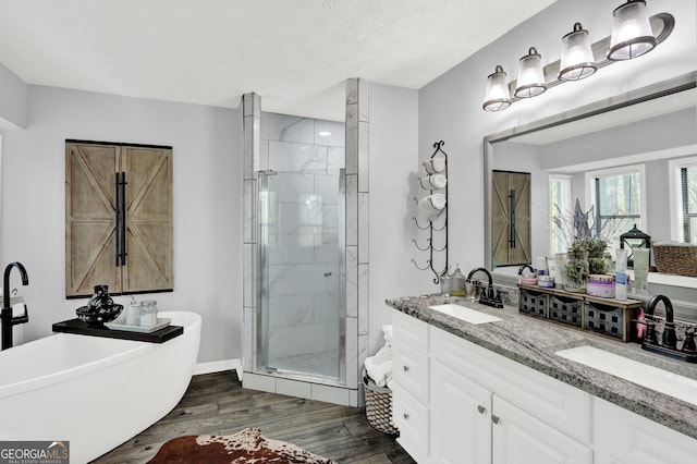 full bath with a stall shower, wood finished floors, a freestanding bath, vanity, and a textured ceiling