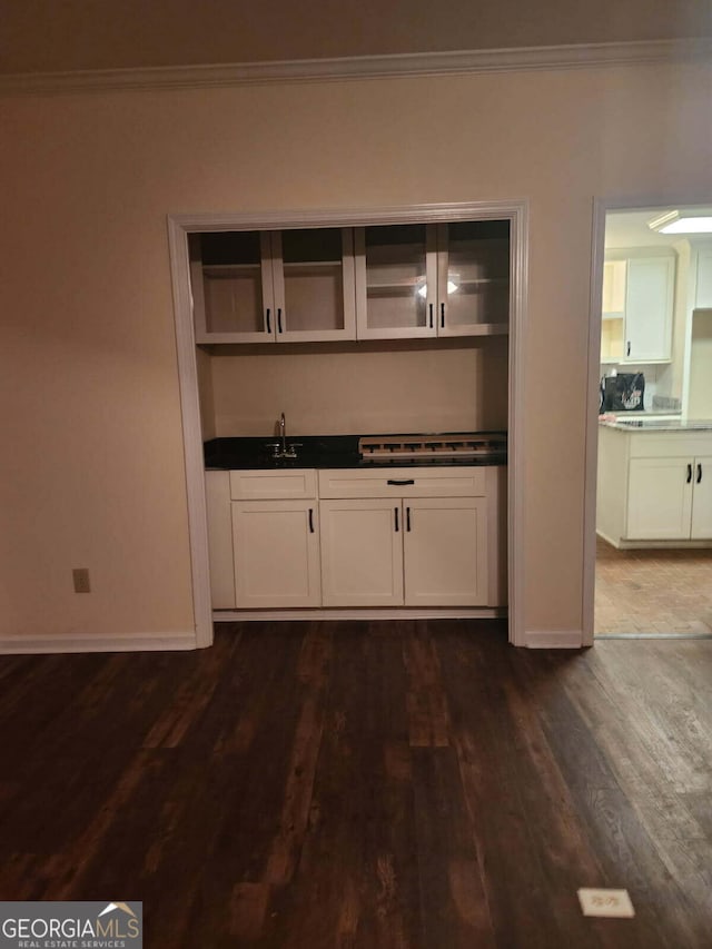 bar featuring dark wood finished floors, baseboards, wet bar, and crown molding
