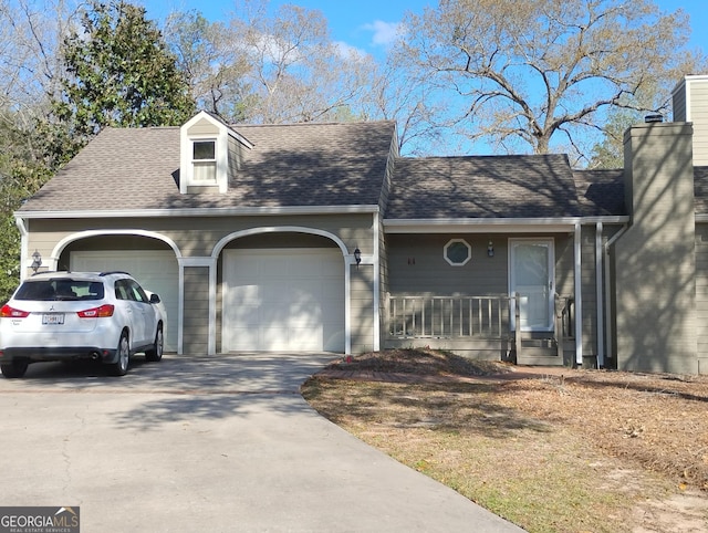 view of front of home with covered porch, a chimney, concrete driveway, roof with shingles, and an attached garage