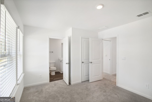 unfurnished bedroom with baseboards, visible vents, carpet floors, and ensuite bath