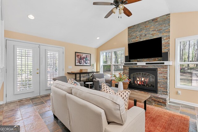 living room with stone tile floors, lofted ceiling, french doors, a ceiling fan, and a fireplace