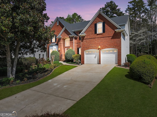 traditional home featuring driveway, an attached garage, brick siding, and a yard