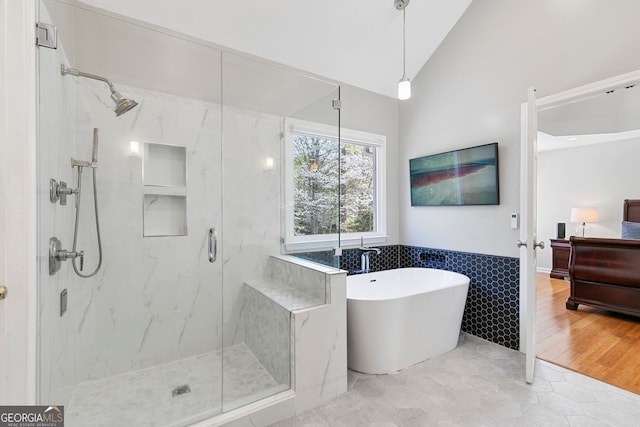 full bath with a freestanding tub, a marble finish shower, tile walls, vaulted ceiling, and a wainscoted wall