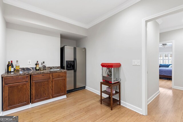 bar with a sink, stainless steel refrigerator with ice dispenser, light wood finished floors, and crown molding