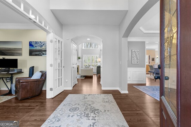 entrance foyer featuring french doors, arched walkways, ornamental molding, and dark wood finished floors