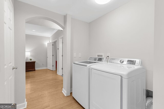 laundry area with light wood-type flooring, baseboards, separate washer and dryer, arched walkways, and laundry area