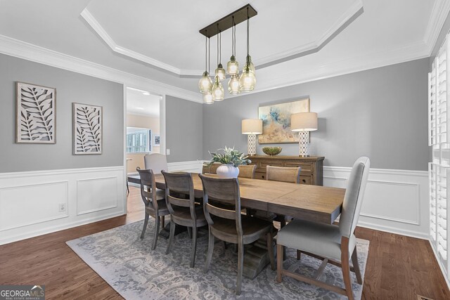 dining room featuring a wainscoted wall, a tray ceiling, crown molding, and dark wood-type flooring