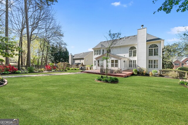back of property with a chimney, a wooden deck, fence, and a yard