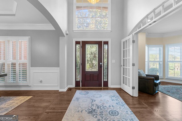 entryway with arched walkways, a wealth of natural light, crown molding, and dark wood finished floors