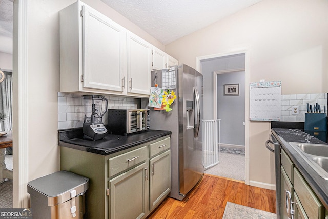 kitchen with tasteful backsplash, dark countertops, light wood-style floors, white cabinets, and appliances with stainless steel finishes