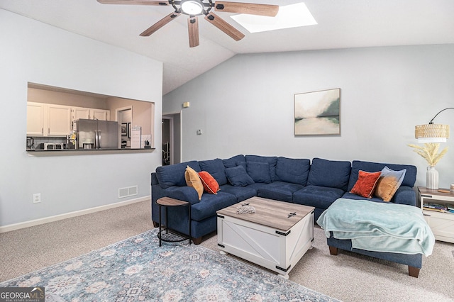 carpeted living area with baseboards, visible vents, vaulted ceiling with skylight, and ceiling fan