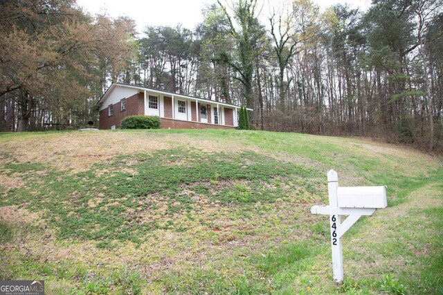 view of front of property featuring covered porch, cooling unit, brick siding, and a front yard