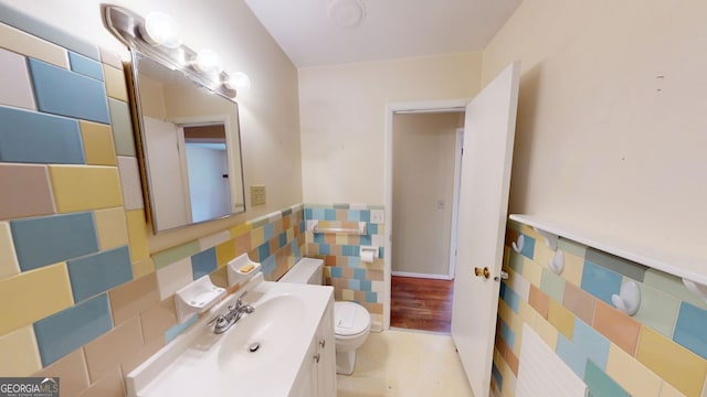 bathroom featuring toilet, tile walls, wainscoting, and vanity