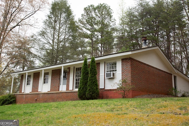 ranch-style house featuring brick siding, a front lawn, a porch, and cooling unit