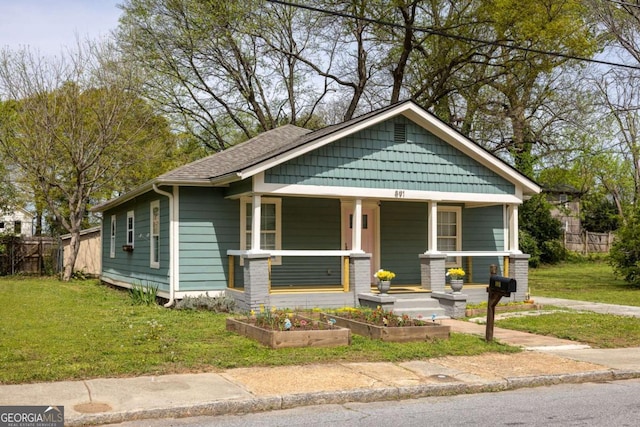 view of front facade featuring a front lawn, covered porch, fence, and a vegetable garden
