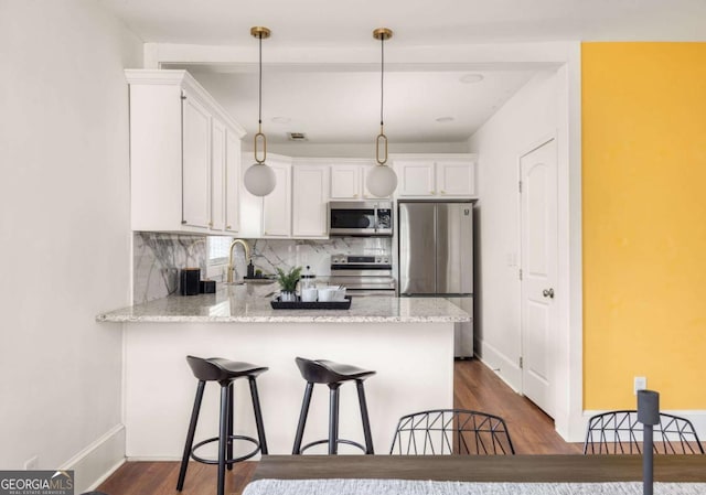 kitchen featuring appliances with stainless steel finishes, a peninsula, dark wood finished floors, white cabinets, and decorative backsplash