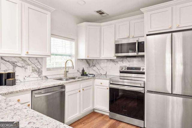 kitchen with visible vents, light wood finished floors, stainless steel appliances, white cabinetry, and a sink