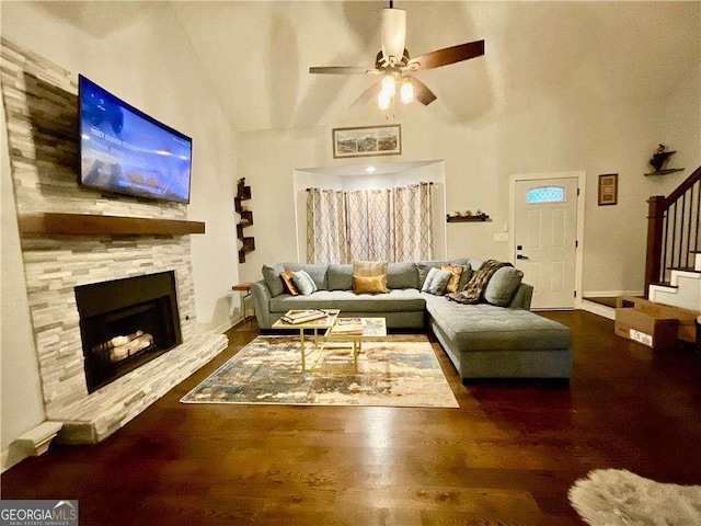 living area featuring stairs, a ceiling fan, a fireplace, wood finished floors, and a towering ceiling