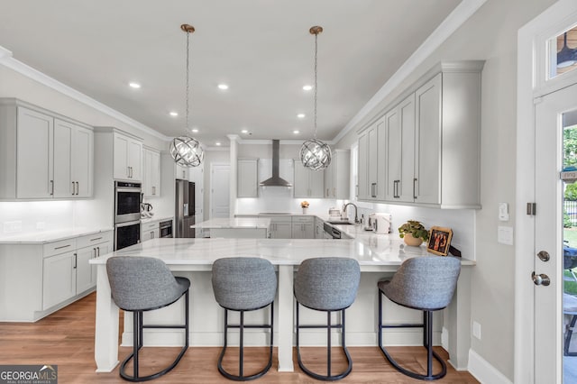 kitchen with a sink, a peninsula, stainless steel appliances, recessed lighting, and wall chimney exhaust hood