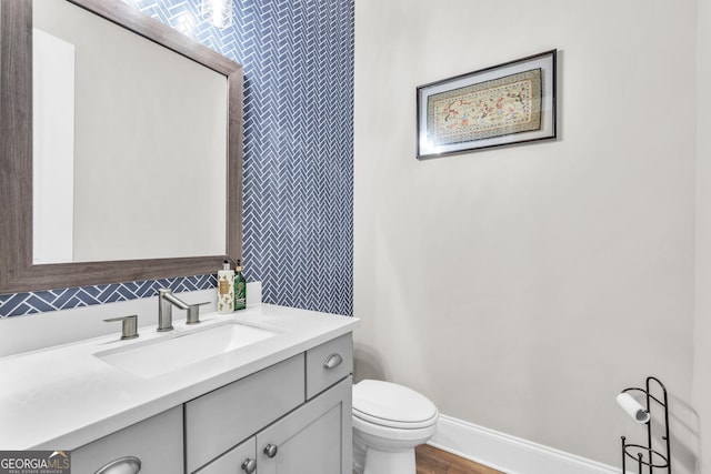 bathroom featuring toilet, baseboards, wood finished floors, and vanity