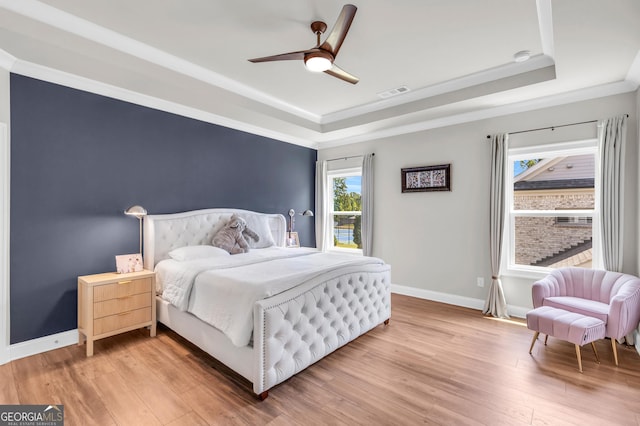 bedroom featuring visible vents, baseboards, a tray ceiling, and light wood-type flooring