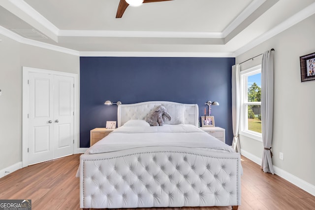 bedroom with ceiling fan, visible vents, wood finished floors, a raised ceiling, and ornamental molding