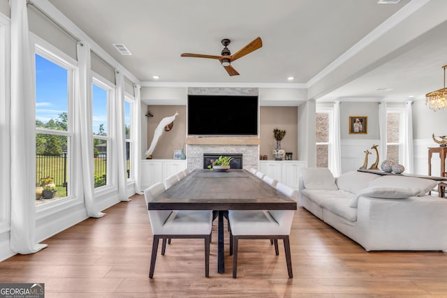living area featuring crown molding, visible vents, a stone fireplace, and ceiling fan with notable chandelier